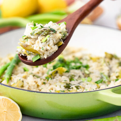 A wooden spoon scooping some lemony asparagus risotto out of the pot.