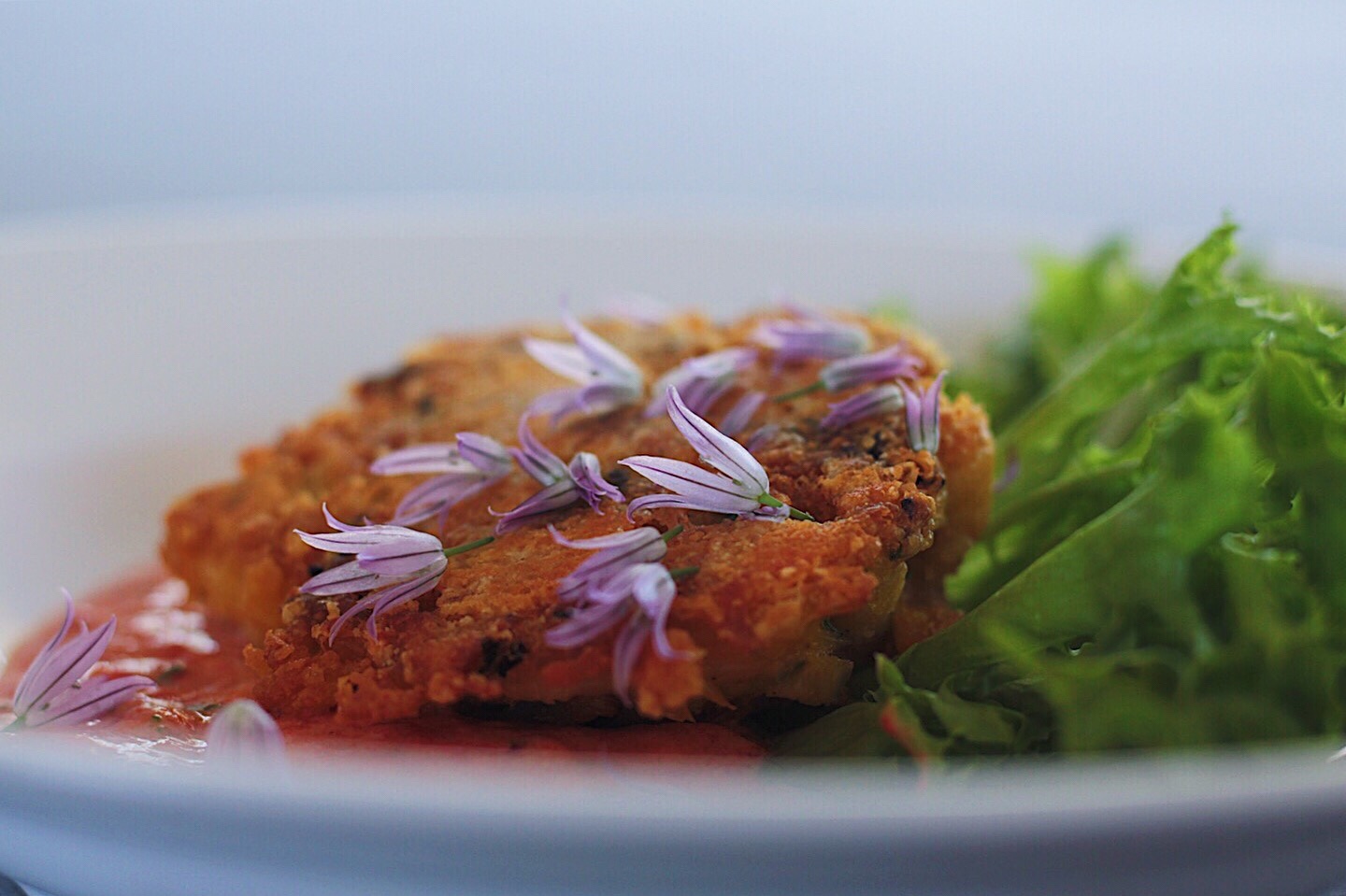 Crab cake with purple chive blossoms and lettuce garnishing.