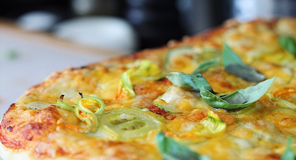 Close up of cooked pizza with pieces of zucchini flowers sprinkled all over the top.