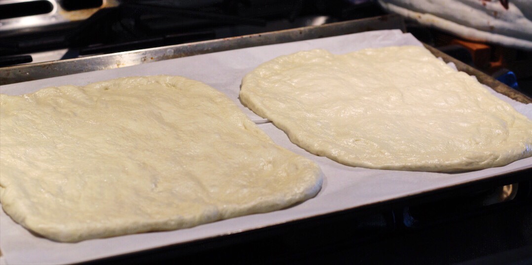 Pizza dough has been rolled out into two rectangles on one large parchment lined cookie sheet. 