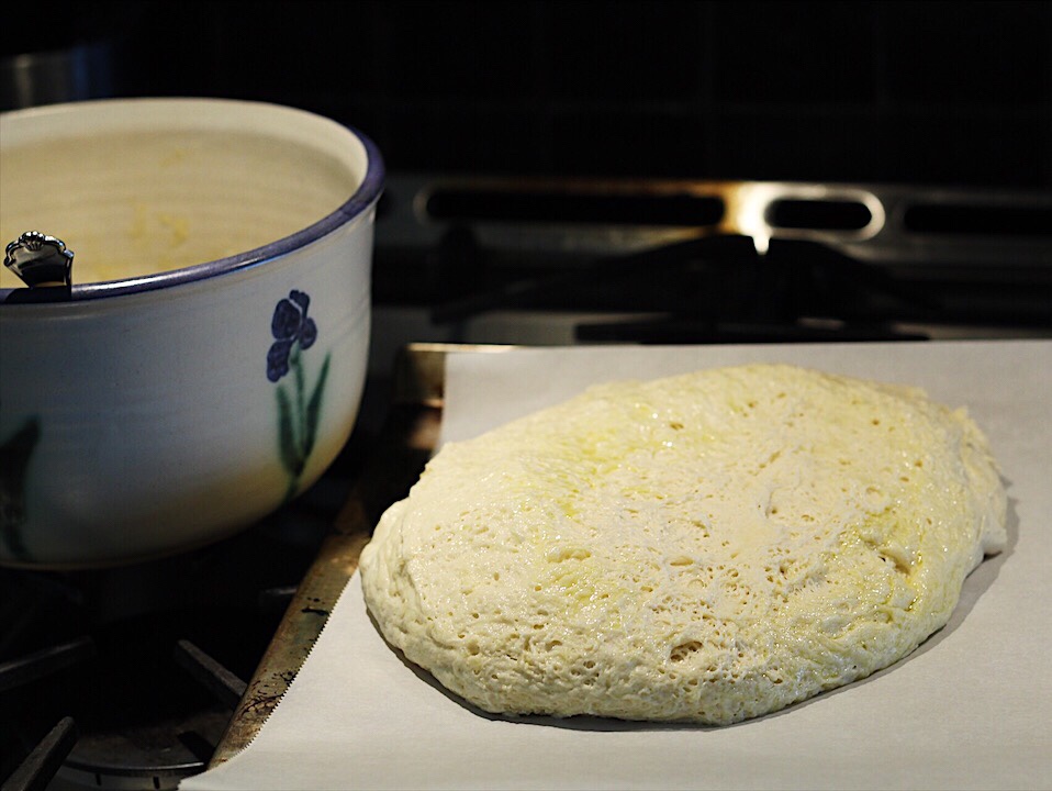 Pizza dough is bubbly after proofing (rising) and has been dumped out of bowl onto parchment lined baking sheet.