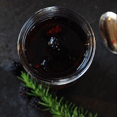 A mason jar full of berries and vinegar with a sprig of rosemary beside.