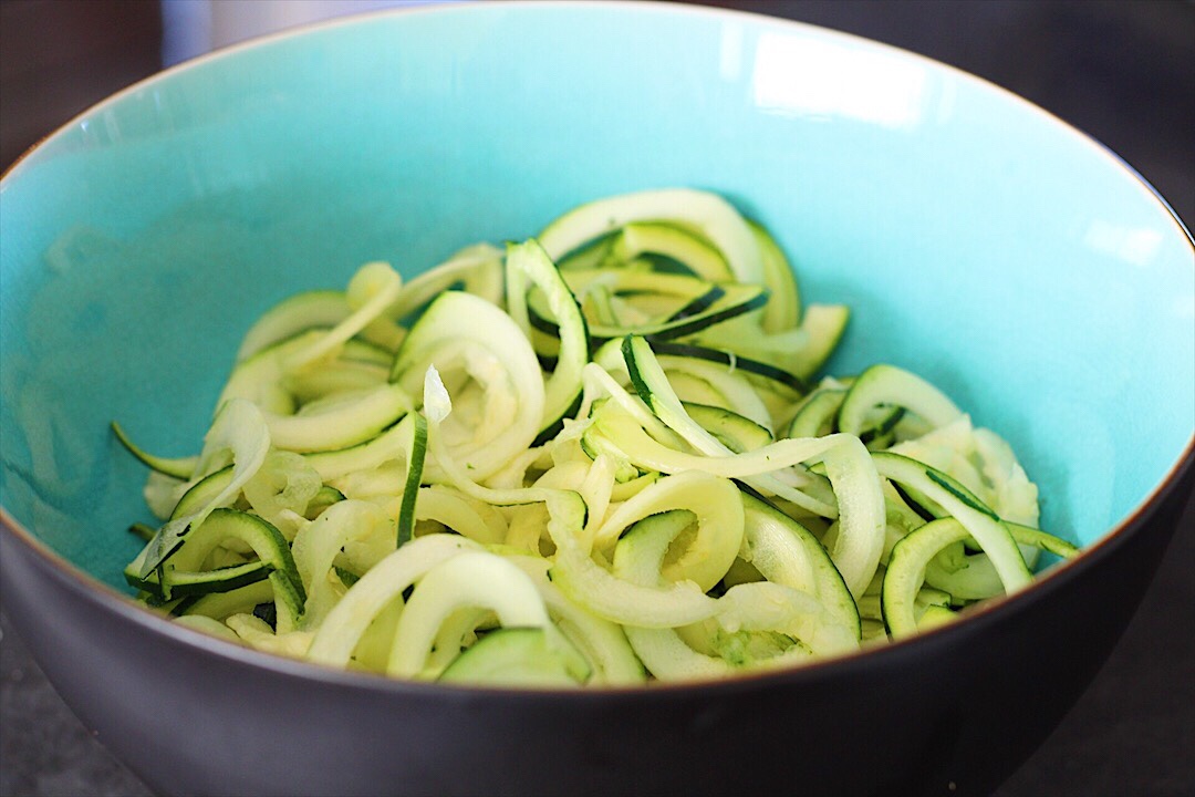 Thinly sliced ribbons of courgette or zucchini in a blue bowl.