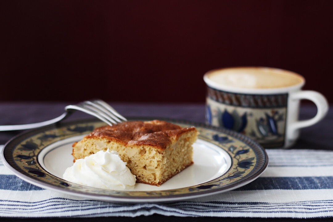 Apple Brown Sugar Cardamom Cake with whipped cream and a cup of coffen.