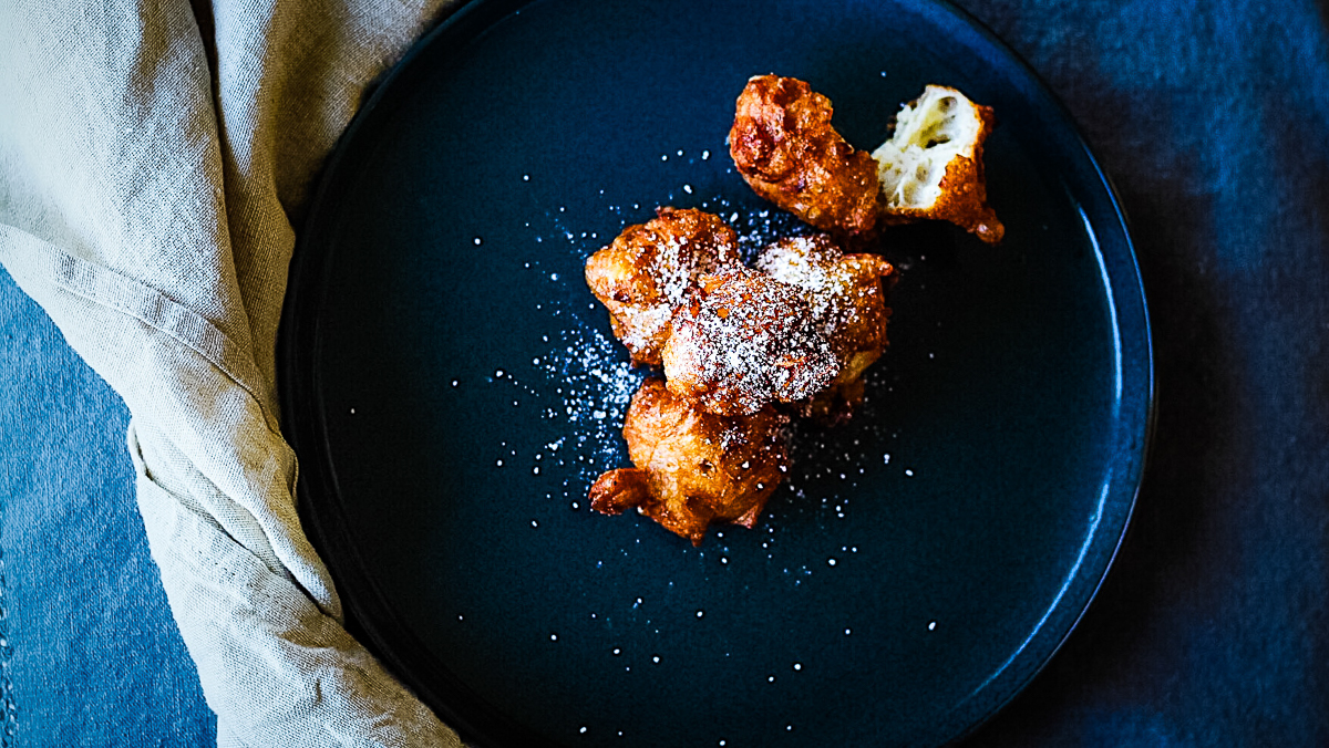 Elegant platter of golden brown, icing sugar dusted fritters.