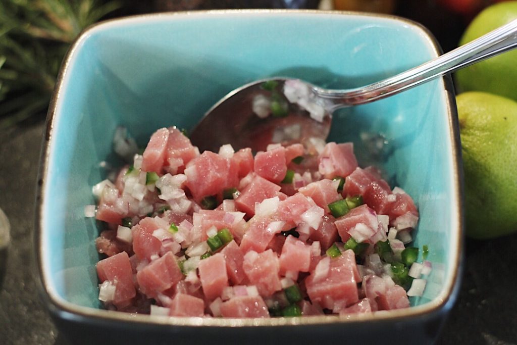 Tuna pieces, diced jalapeno and onion are stirred together in a blue bowl.