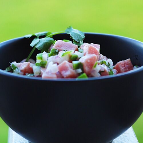 Black bowl filled with cubed tuna ceviche and cilantro and a green background.