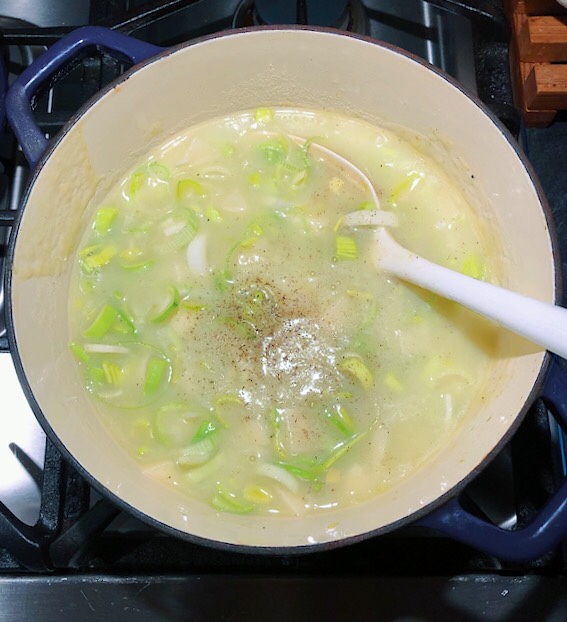 Leeks and water simmer for soup with a ladle in the pot. 