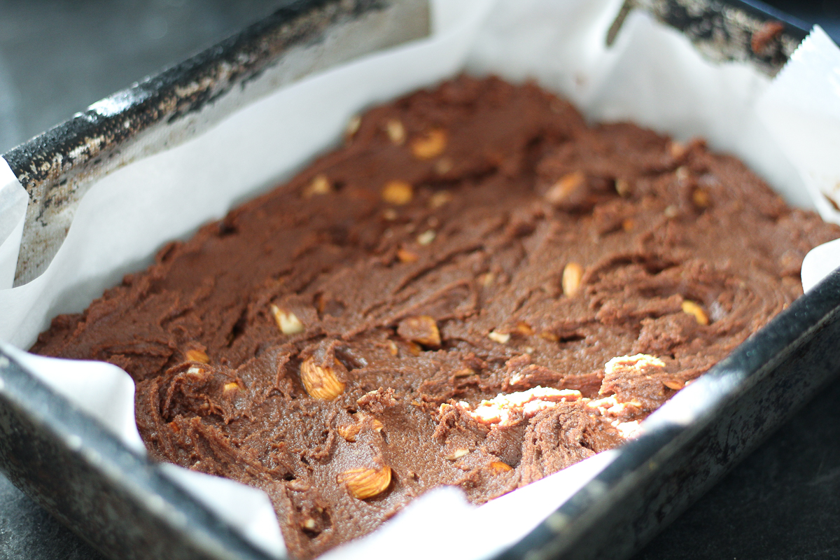 Almond brownie batter, raw in parchment lined baking pan.