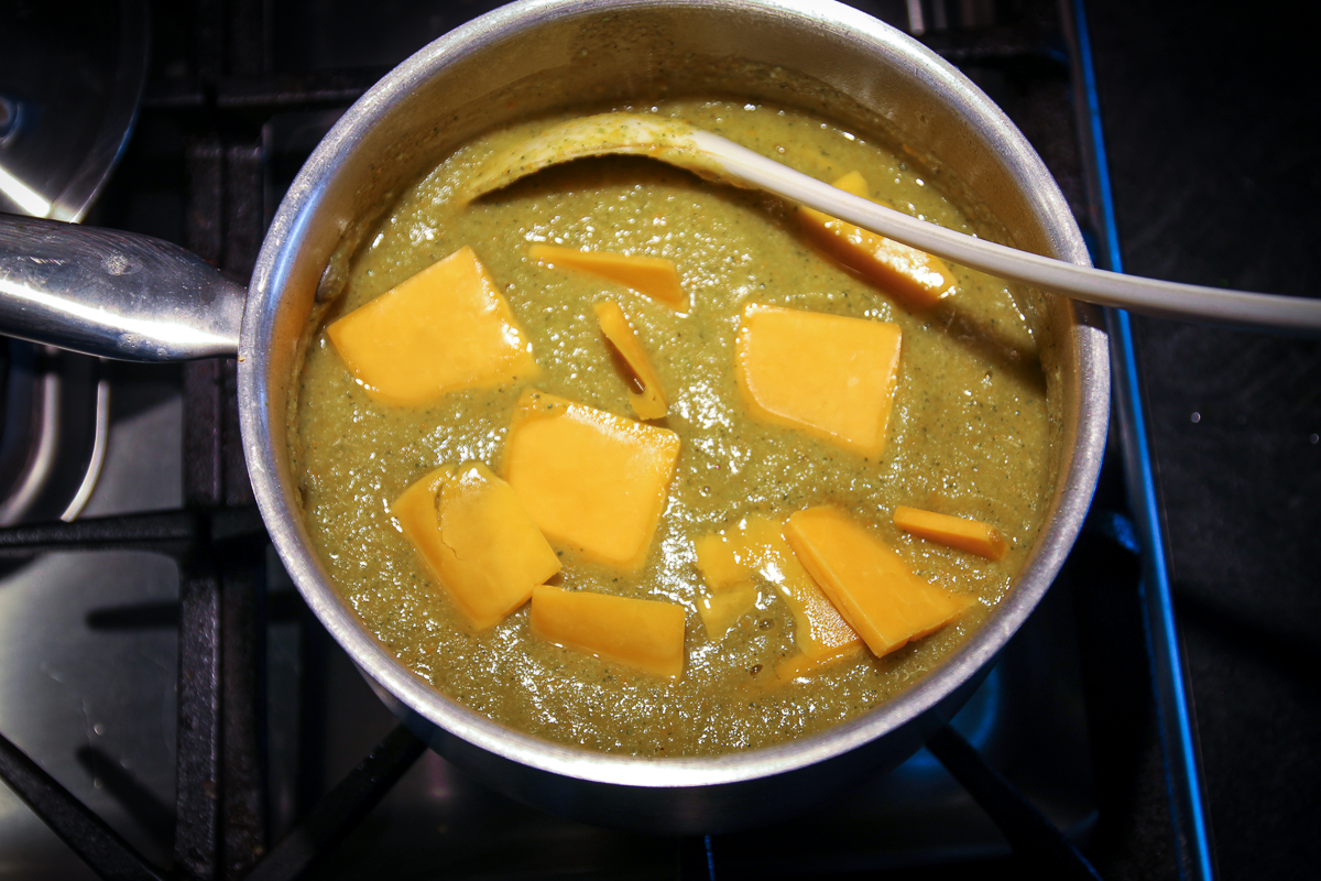 Thin slices of cheddar cheese are added to the soup and starting to melt.
