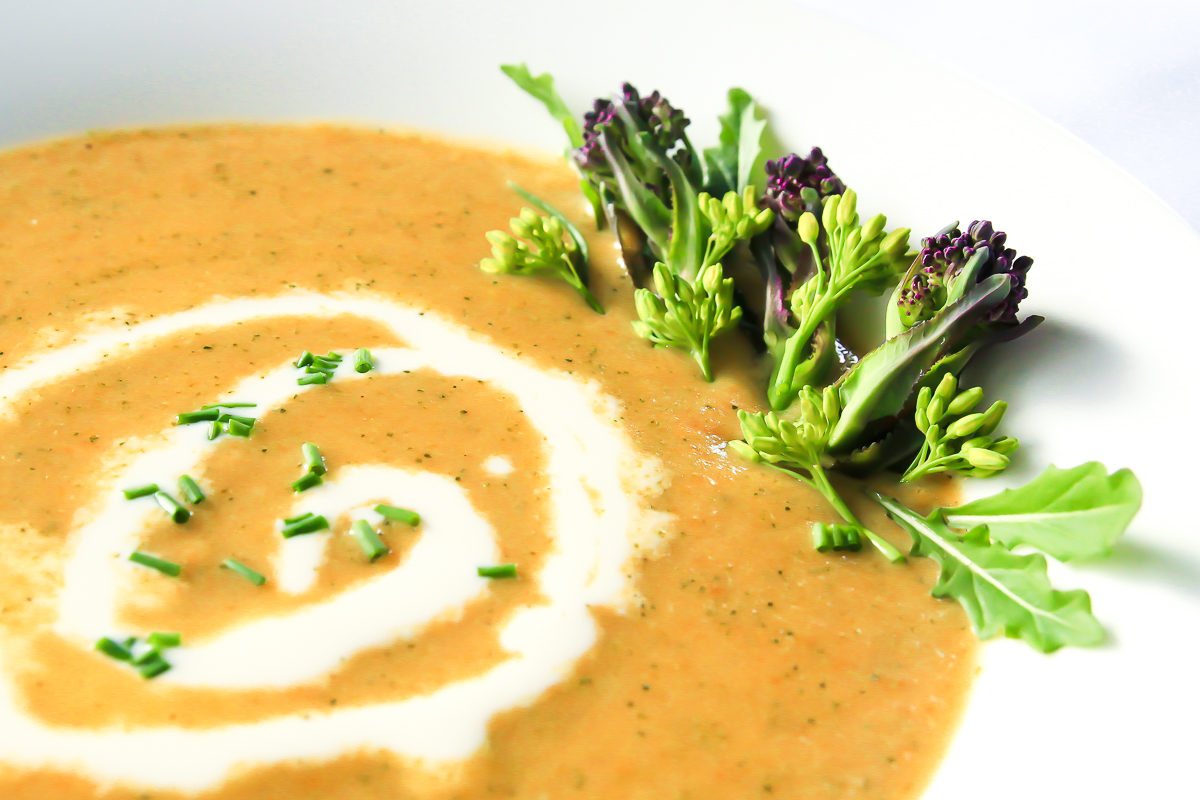 Close up of orange broccoli cheese soup with white swirl of cream and broccoli florets garnishing.