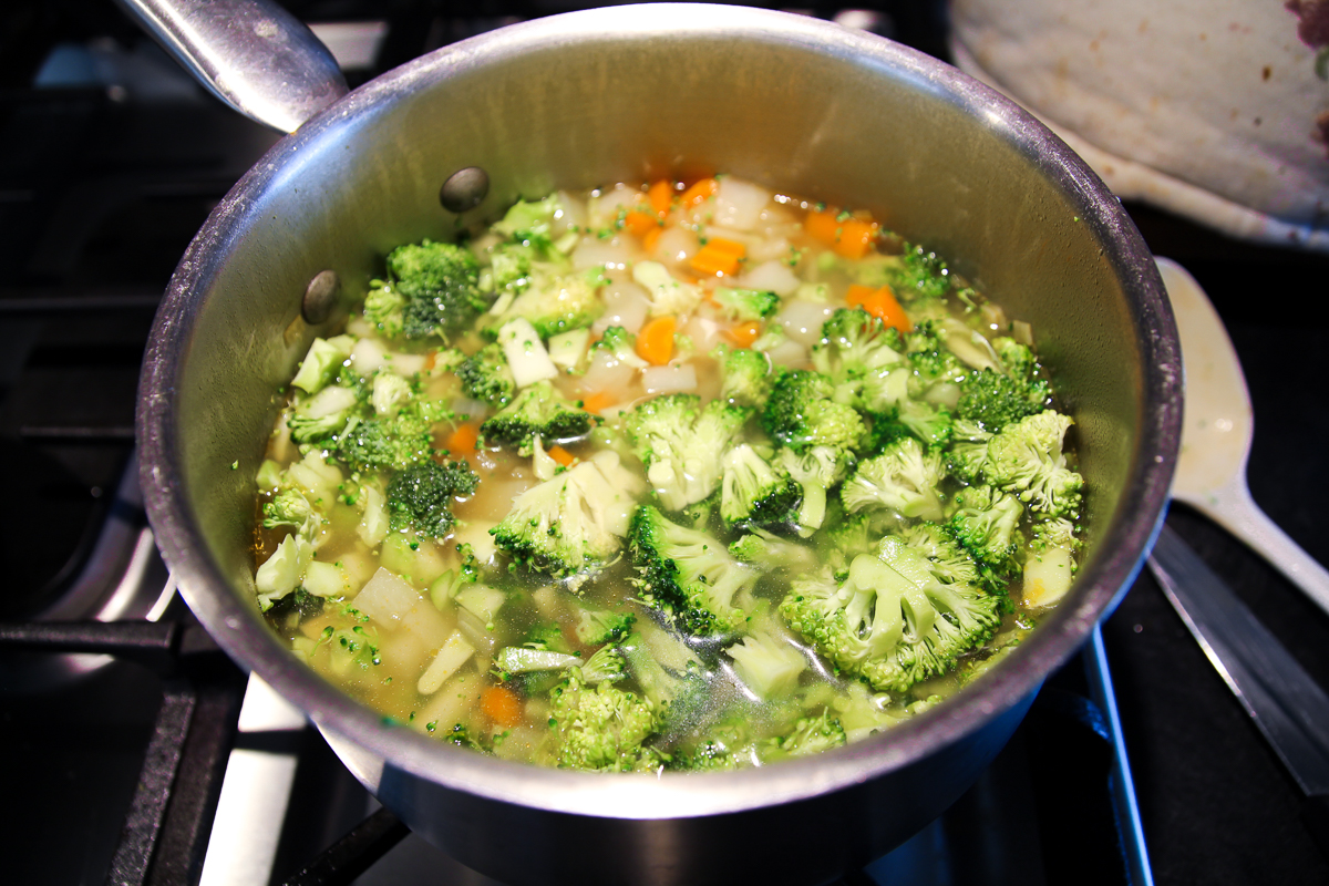 Diced carrot, onion, potato and broccoli simmering in a stainless steel pot for soup.