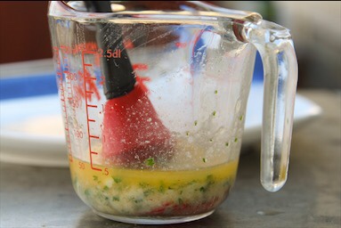 Glass measuring cup with melted butter, garlic and parsley.