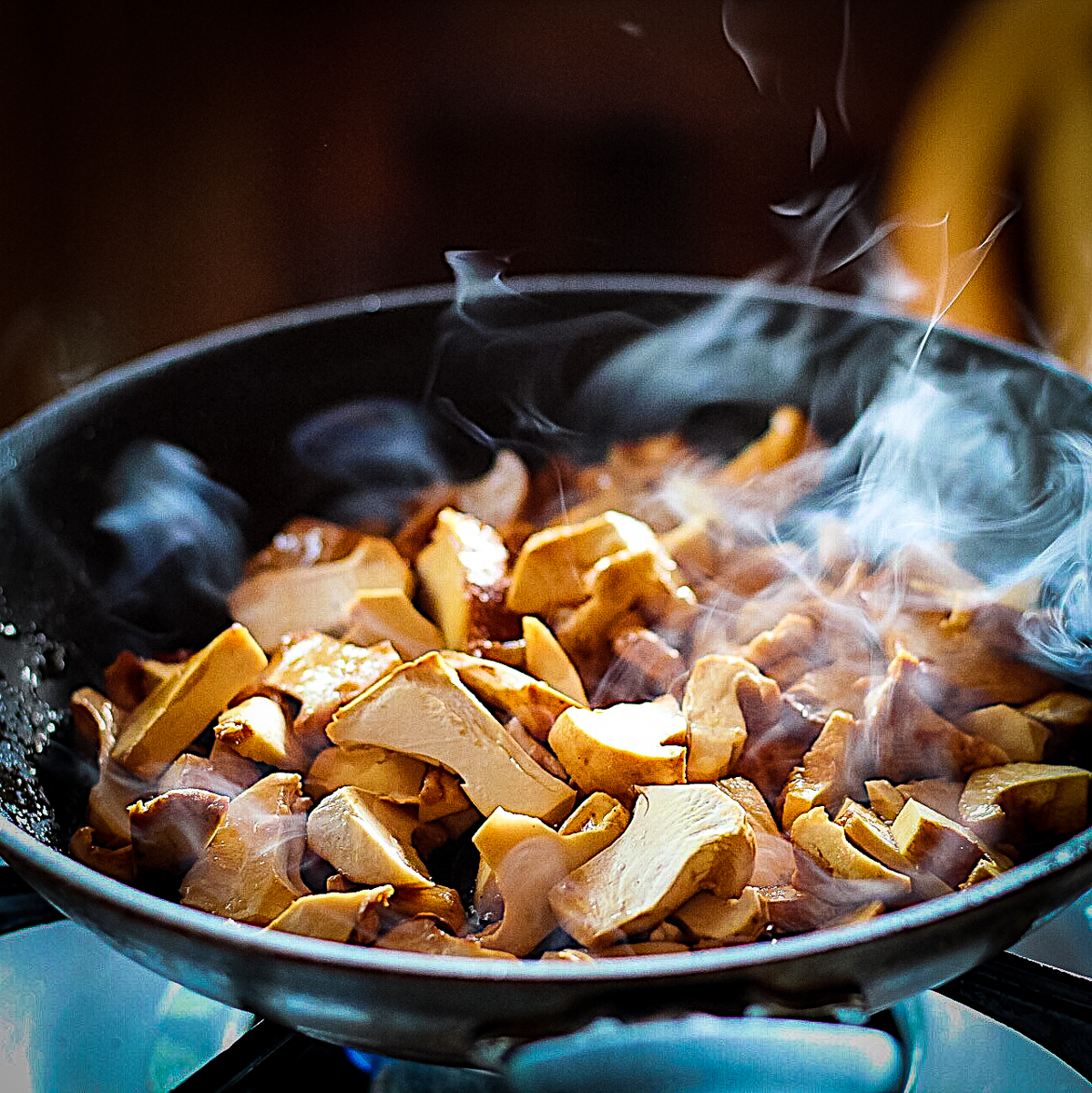 Chanterelle mushrooms frying in a black pan. Steam is rising off the pale orange mushrooms.
