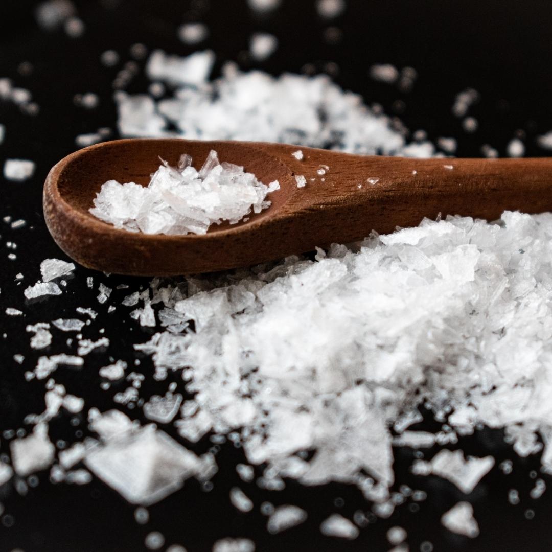 Closeup of crunchy kosher sea salt with a small wooden spoon on a black countertop.