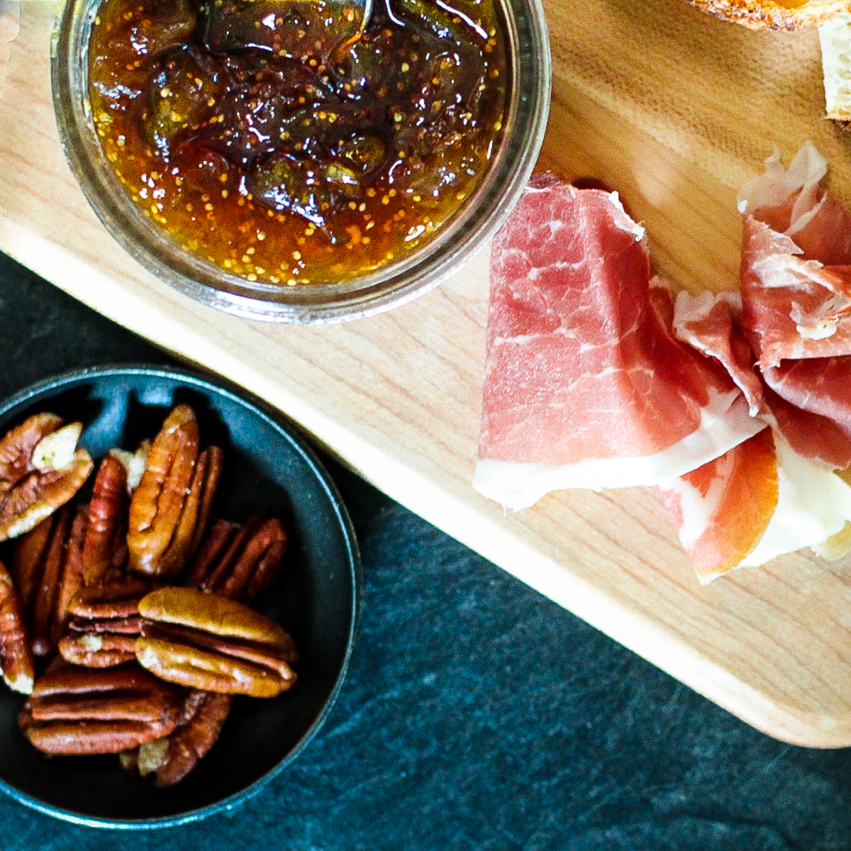 Fig jam in jar beside prosciutto and pecans