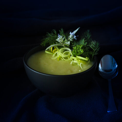 Dark background and black bowl with pale green leek potato soup for winter.