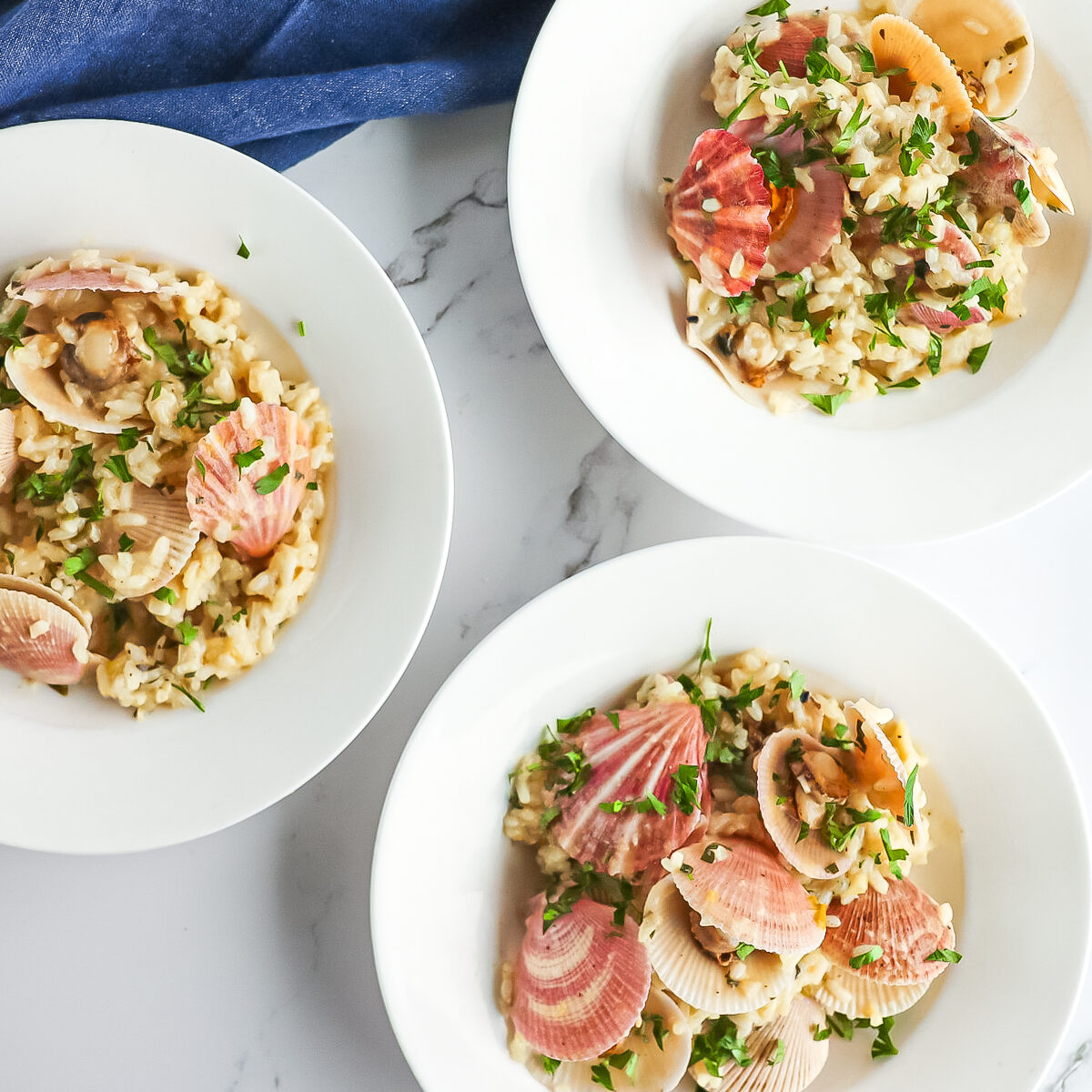 3 white bowls with creamy risotto, pink scallop and green herbs garnishing.