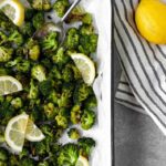 White 9x13 pan of roasted broccoli florets and slivers of lemon.