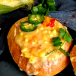 A bread bowl with the top cut off. It is filled with a creamy cheesy soup and garnished with sliced jalapenos and cilantro.
