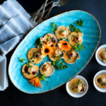 Pink Scallops broiled on the half shell with creamy sauce. They are sitting on a bright blue platter decorated with orange calendula.
