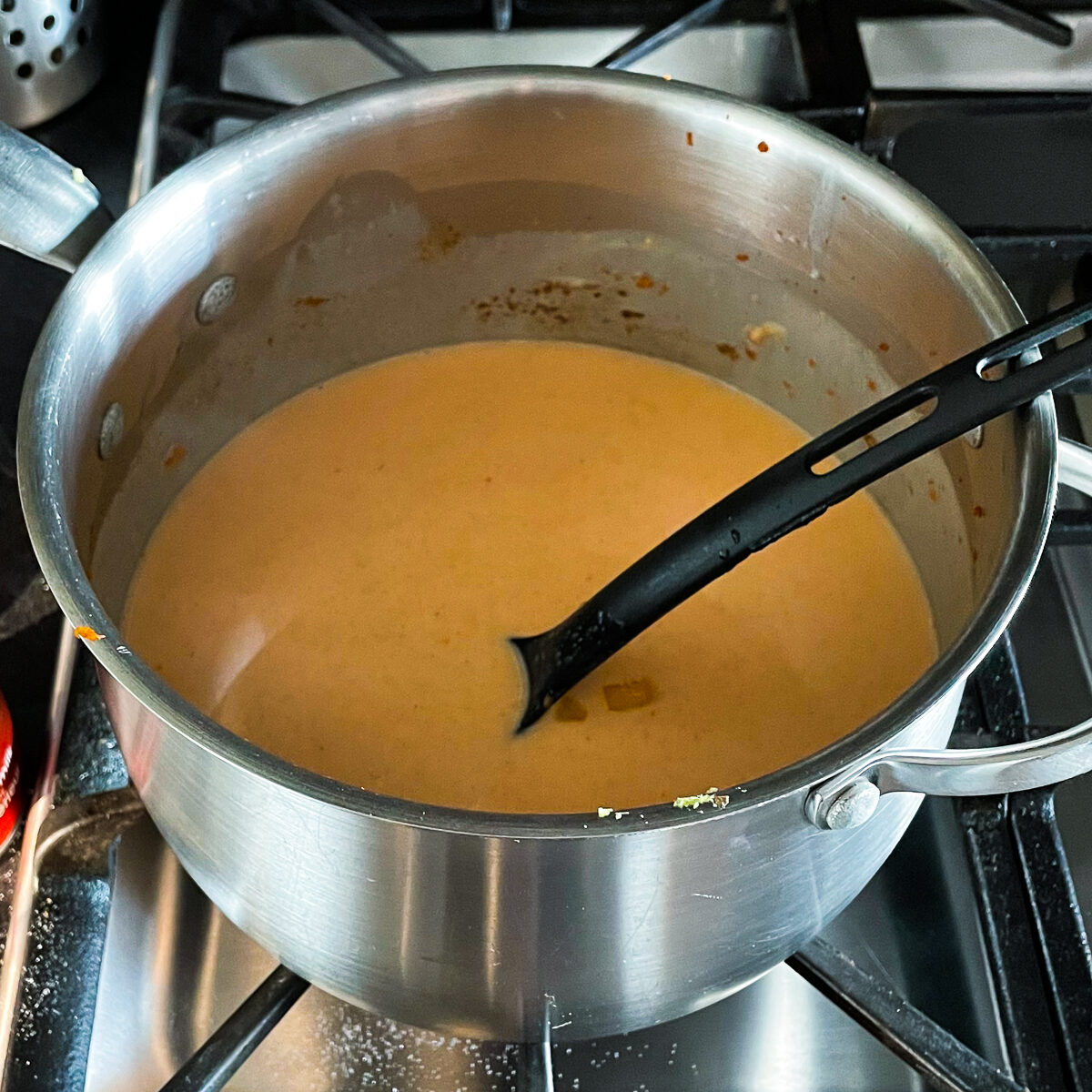 Orange pink coconut curry broth simmering in a pot with a black spoon in it.