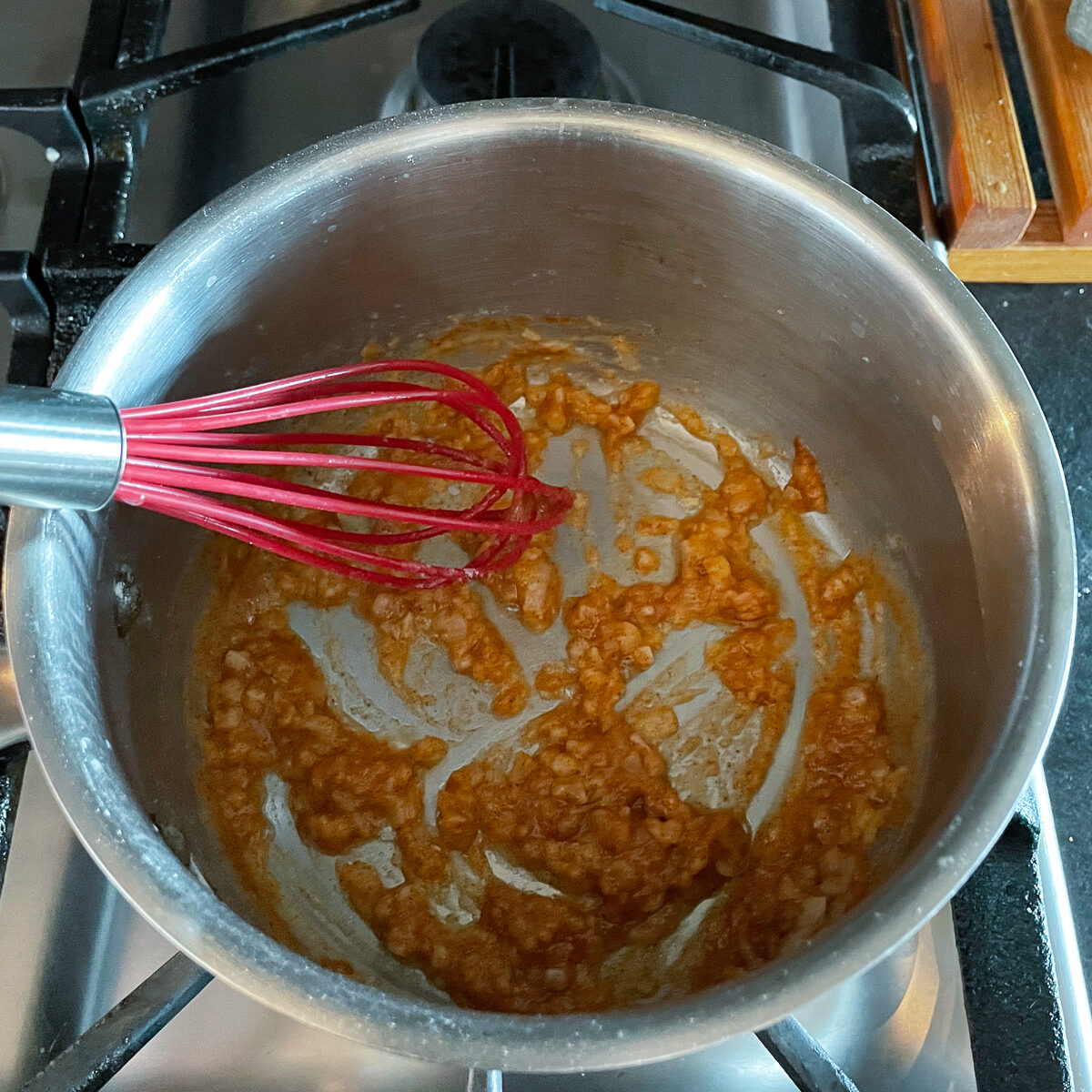The flour, paprika and onion has created an orange paste that is cooking in the saucepan.