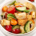 White bowl with large croutons, tomatoes and cucumber for panzanella salad.