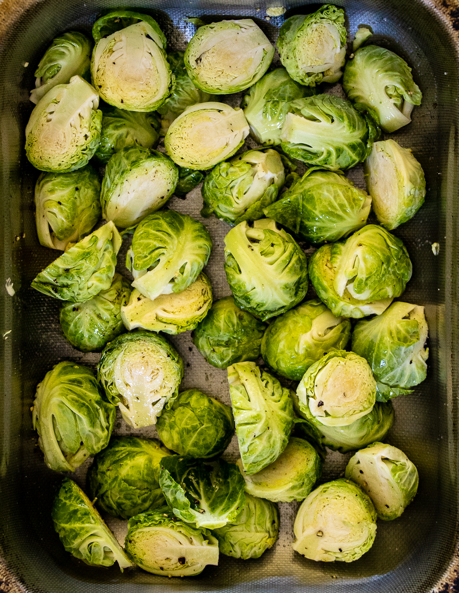 Trimmed and halved Brussels sprouts in dark silver roasting pan.