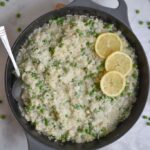 A cast iron pan full of white risotto with green peas stirred in and slices of lemon garnishing the top.