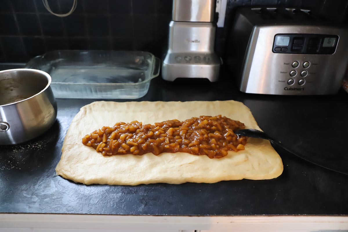 The cooled apple pie filling is poured along the middle of the dough rectangle.