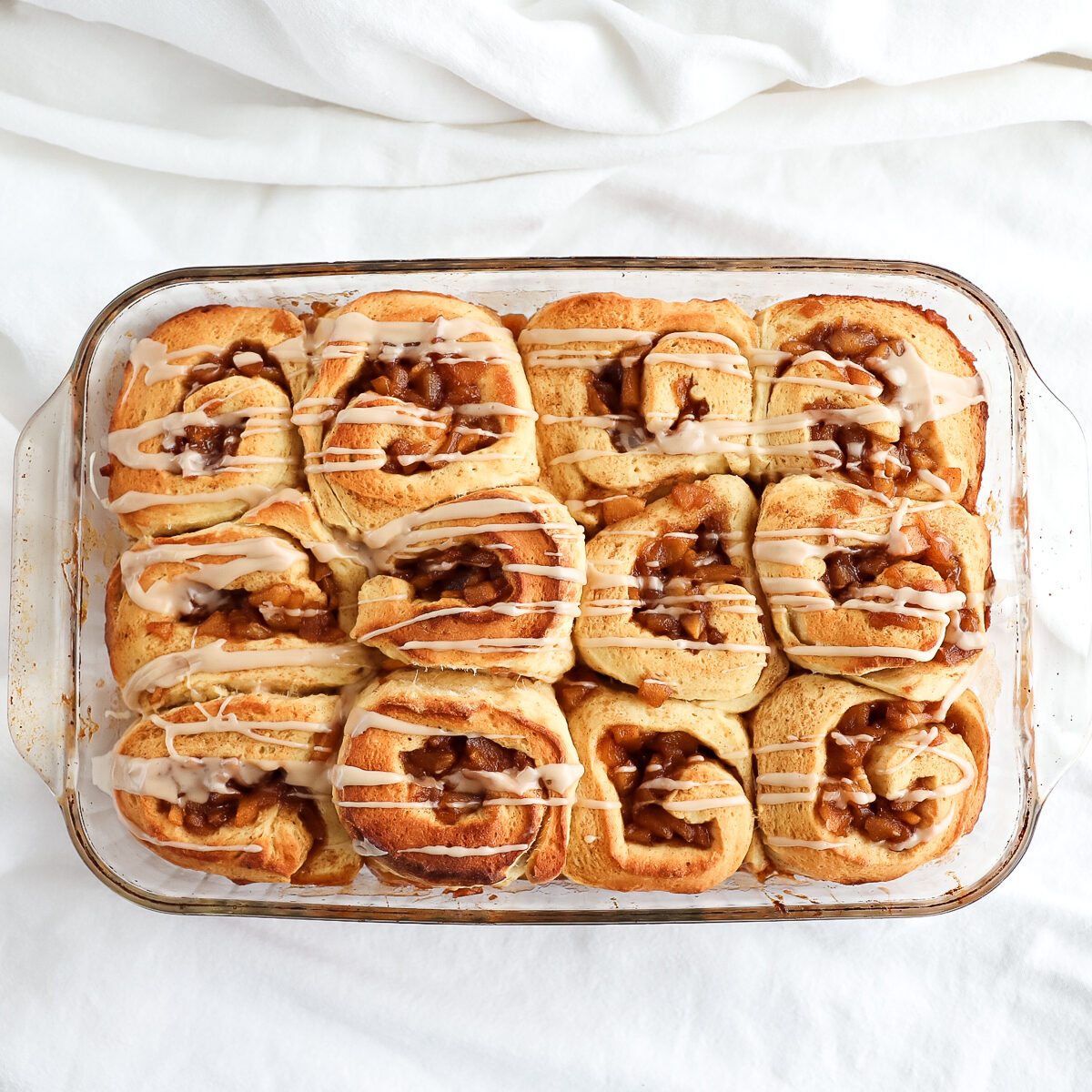 9 x 13 inch glass pan with 12 baked cinnamon buns in it. They have pale icing drizzle over horizontally.