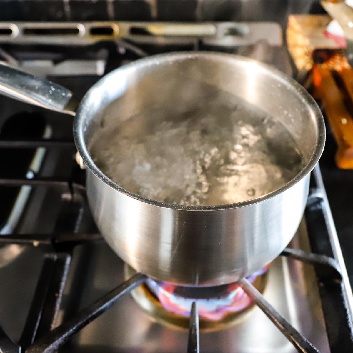 A pot of water boiling over the flame on a gas stove.