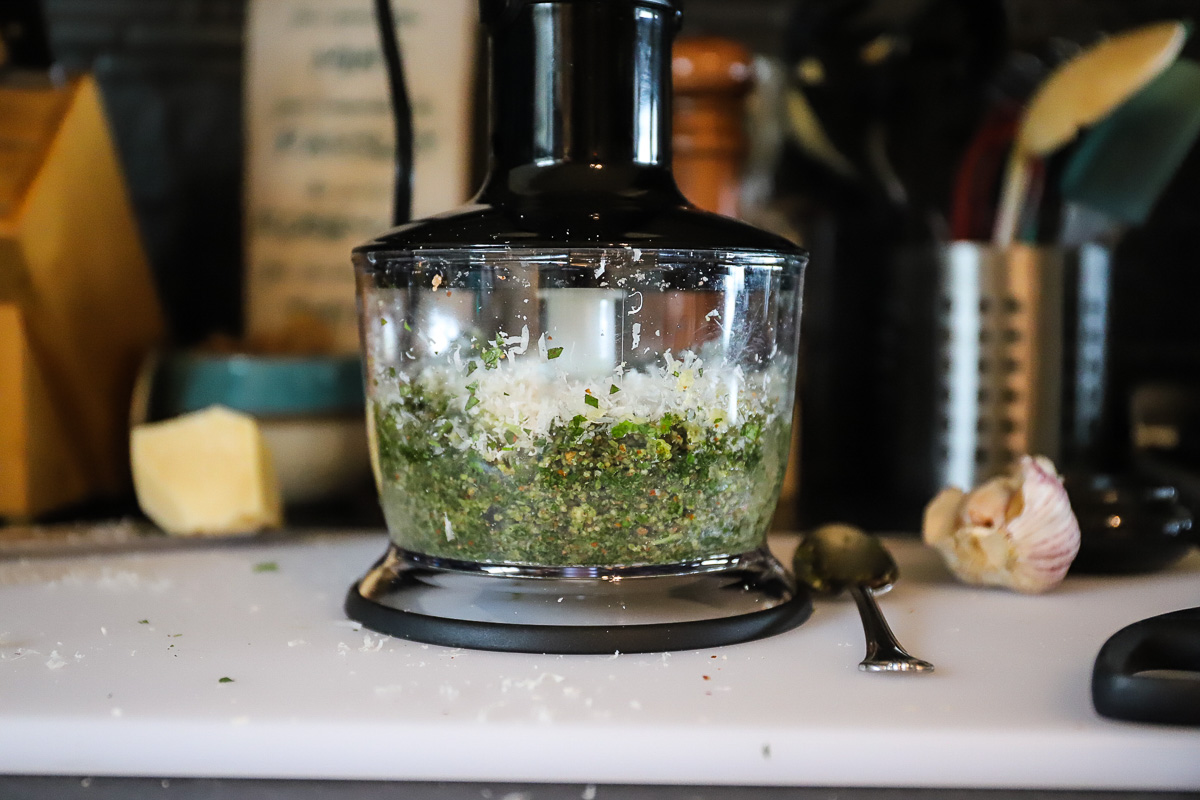 The green puree in the food processer has grated parmesan on top ready to blend. The lid is on the processor.