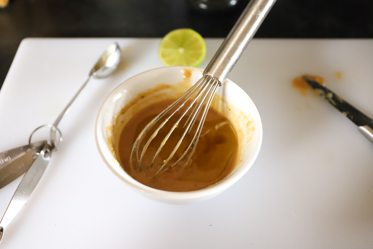 The creamy brown dressing has the olive oil added on top with the whisk in it.