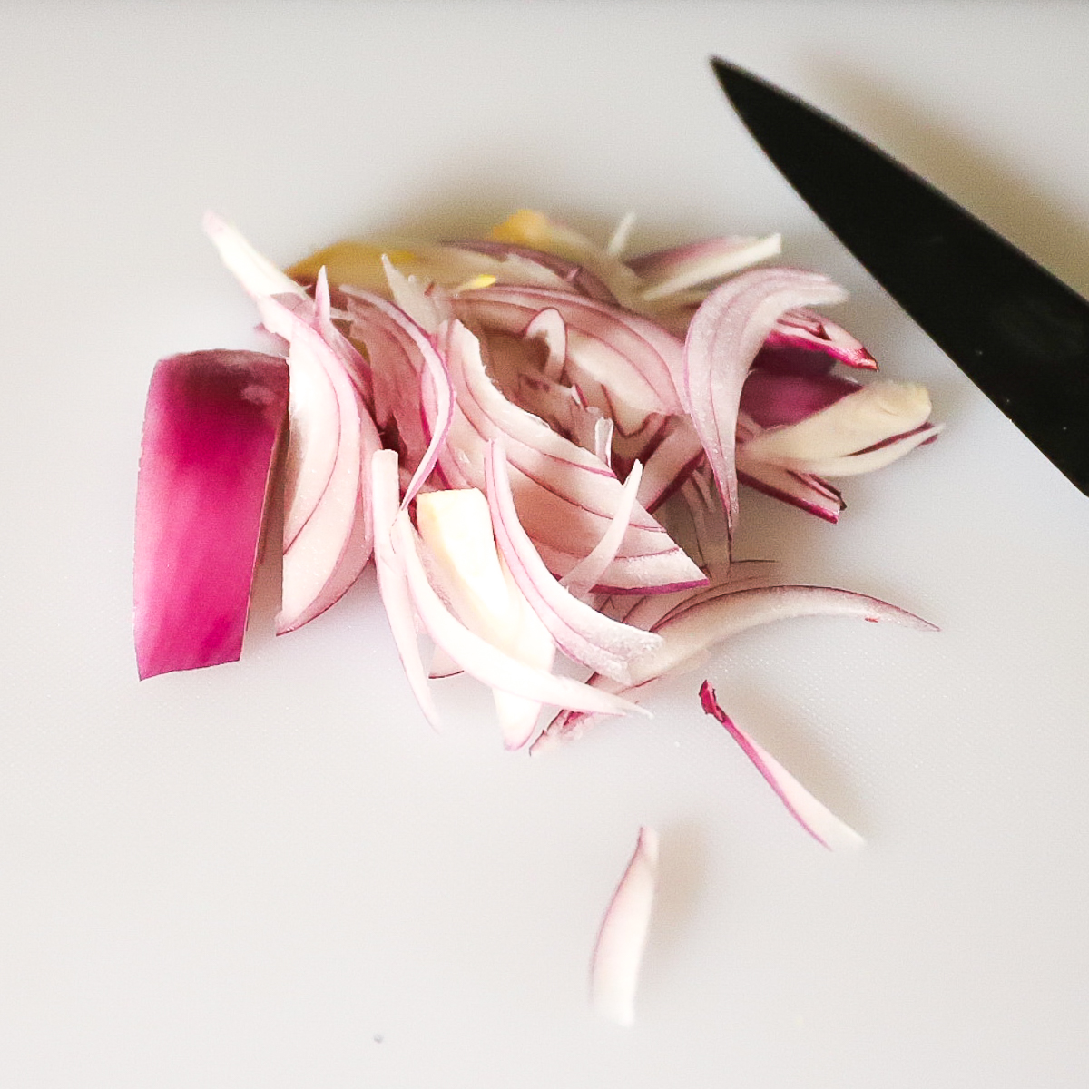 Red onion that has been sliced very thinly with a knife beside the pieces.