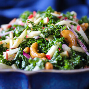 Close up front view of colorful kale and apple salad showing the cashews and purple onion slices.