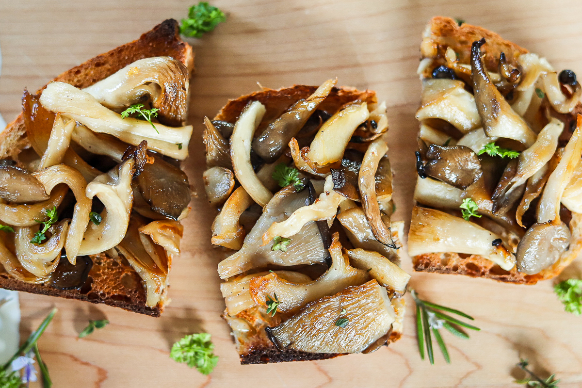 Overhead shot of fried oyster mushrooms on a piece of toast cut in 3 pieces. It is on a wooden cutting board with bits of parsley around it.
