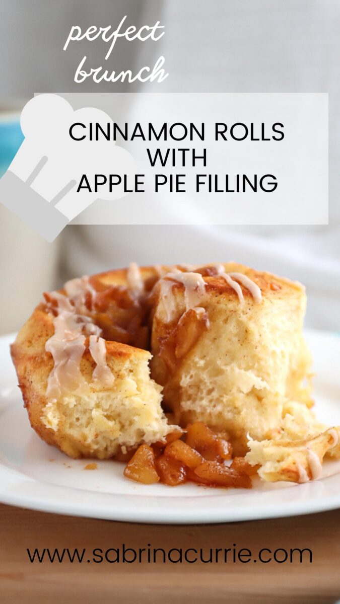 Close up picture of a single cinnamon roll with the apple pie filling spilling out. It is on a white plate that's on a wooden cutting board and there is text overlay of the recipe name.