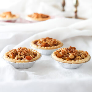 Apple crumble tartlets on a table with white tablecloth and silver candlesticks in the background.