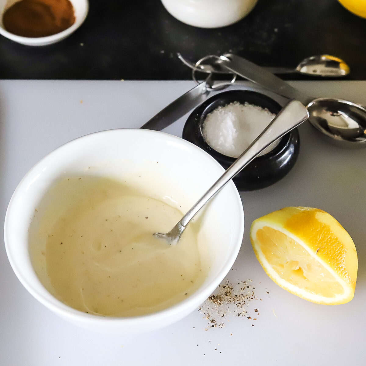 Light yellow creamy sauce in white bowl with used lemon half beside it and salt in the background.