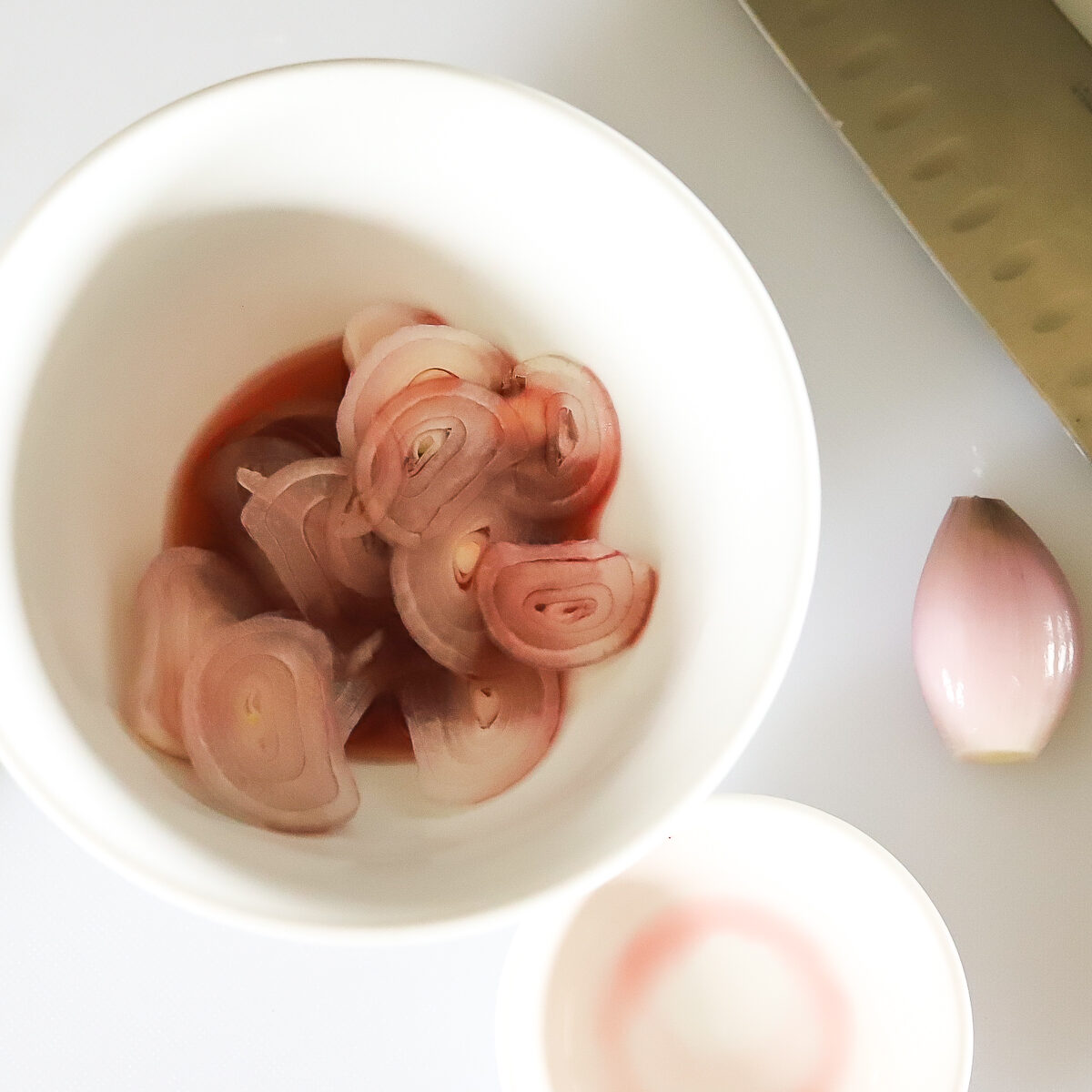 White bowl with thinly sliced shallots and red wine vinegar in it. 