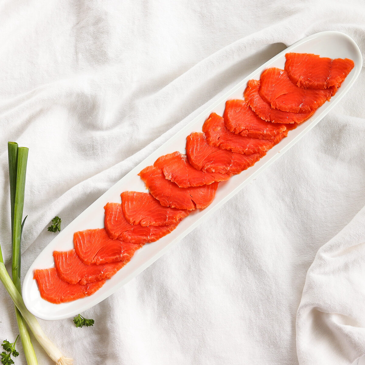 A long white skinny serving platter with thinly sliced salmon along it.
