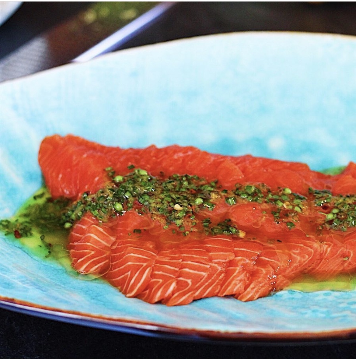 Sliced raw salmon on a blue plate with green citrus herb dressing spooned over top.