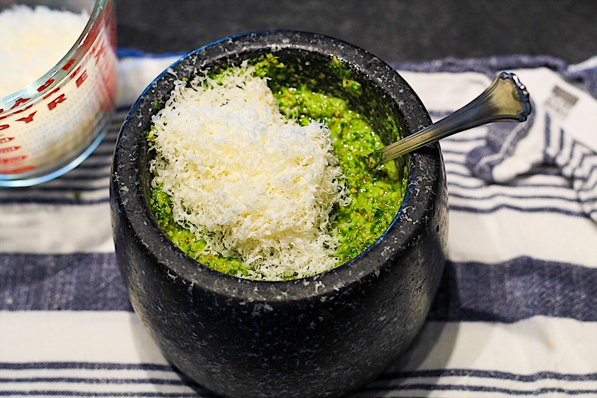 The green pesto in the black bowl has fresh grated parmesan on top, ready to be stirred in.