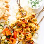 A tangle of bright orange colored tandoori chicken skewers with a side of yogurt dip.