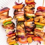 4 grilled skewers with chunks of pineapple, green and orange peppers and chicken on a white plate.