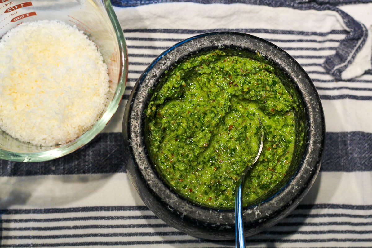 Green pesto in a black mortar with grated parmesan in a measuring cup beside it.