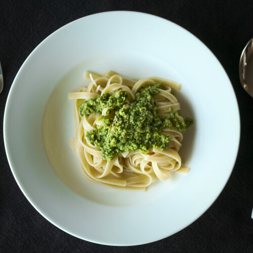 White bowl on black table with fettucine topped with green sorrel pesto on top.