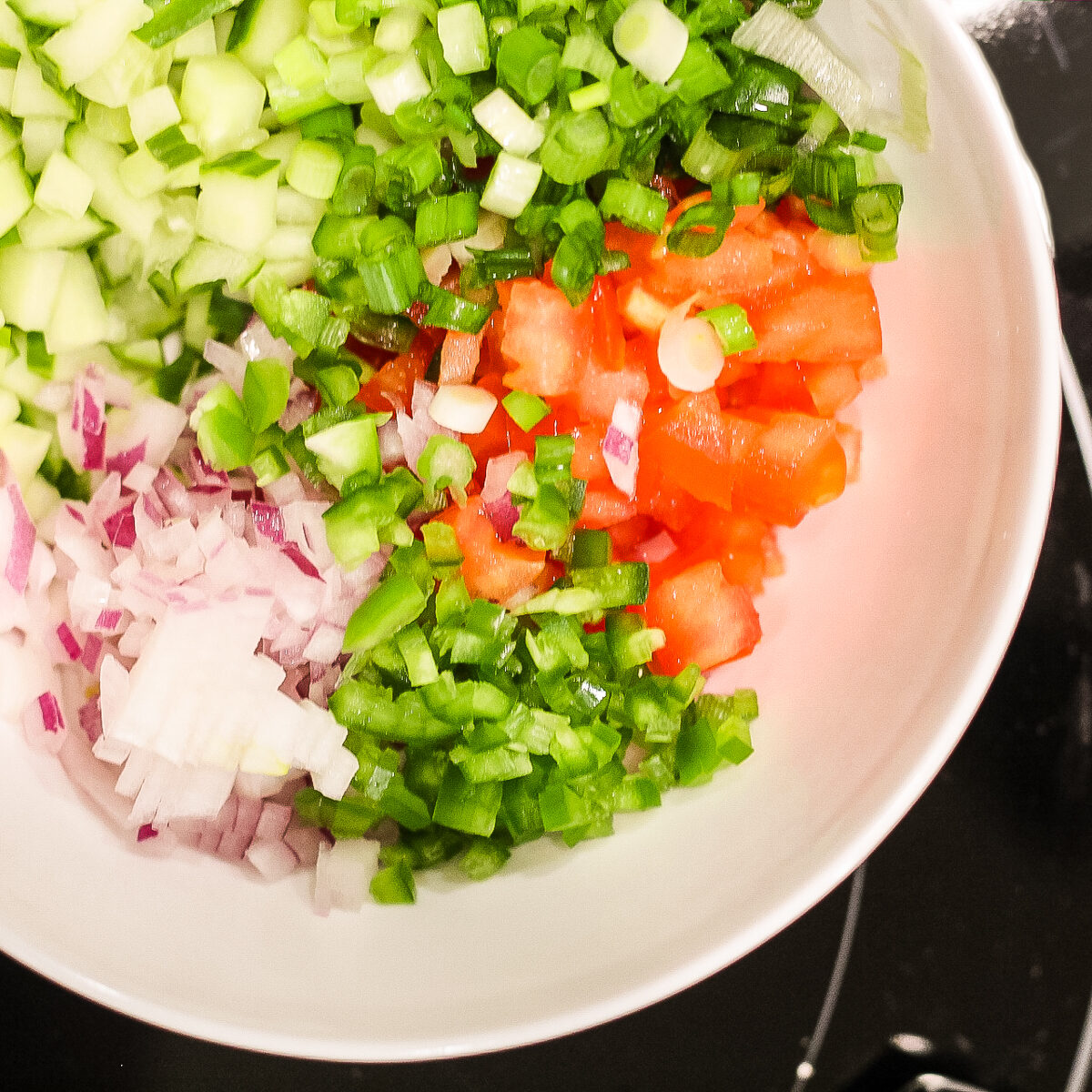 Evenly small diced cucumber, green onion, tomato, green pepper and red onions in a white bowl.